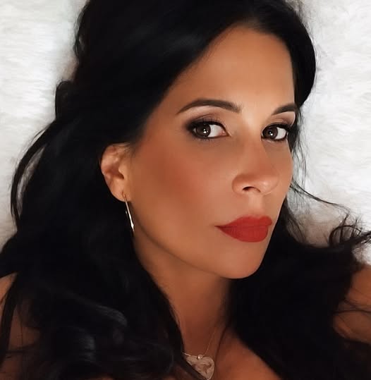 Gaby Ramírez in a close portrait, dark hair and red lipstick, on a pale background.